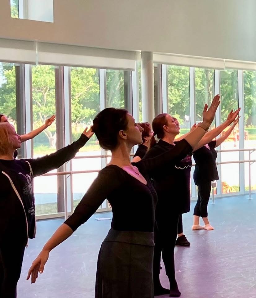 Adult ballet dancers practicing port de bras in a bright dance studio