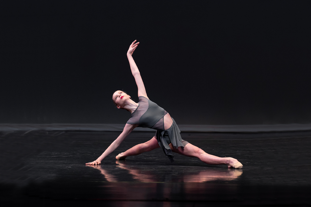 Woman in a ballet position holding herself up with 1 arm on the ground